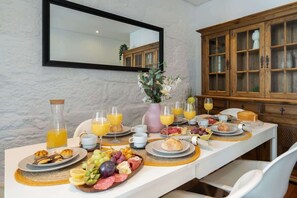 A breakfast table set with plates of food, glasses of orange juice, and a vase of flowers. - Rustic Central Flat | Terrace by Host Wise (Porto)