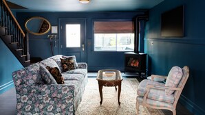 Ein Wohnzimmer mit floralem Sofa, Sesseln in Karomuster, einem kleinen Tisch, einem Kamin und einer Treppe.