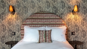 Ein Bett mit einem gemusterten Kopfteil, zwei Wandlampen und ein kleiner Tisch daneben.