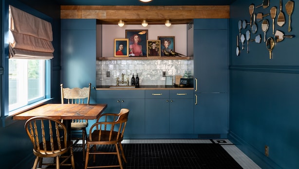 Eine Küche mit blauen Schränken, einem Holztisch und Stühlen. An der Wand hängen Bilderrahmen und es sind verschiedene Küchenutensilien ausgestellt.