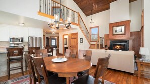 A spacious living area with a wooden dining table, chairs, a fireplace, and a staircase leading to an upper level.