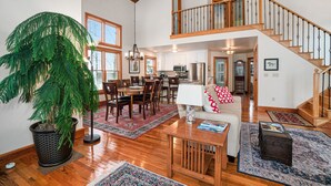 A spacious living area with a dining table, a large potted plant, and a staircase leading to an upper level.