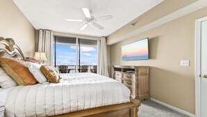Une chambre avec un grand lit, un ventilateur de plafond, un téléviseur fixé au mur et une vue sur l’océan par la fenêtre.