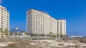 Un hôtel de grande hauteur doté de nombreux balcons, offrant une vue sur la plage et donnant sur une étendue de sable.