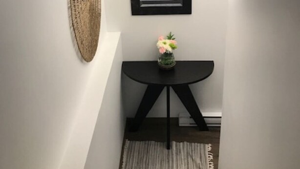 Eine Treppe mit dunkler Holzvertäfelung, ein schwarzer runder Tisch mit einer Blumenvase und ein gewebter Wandbehang.