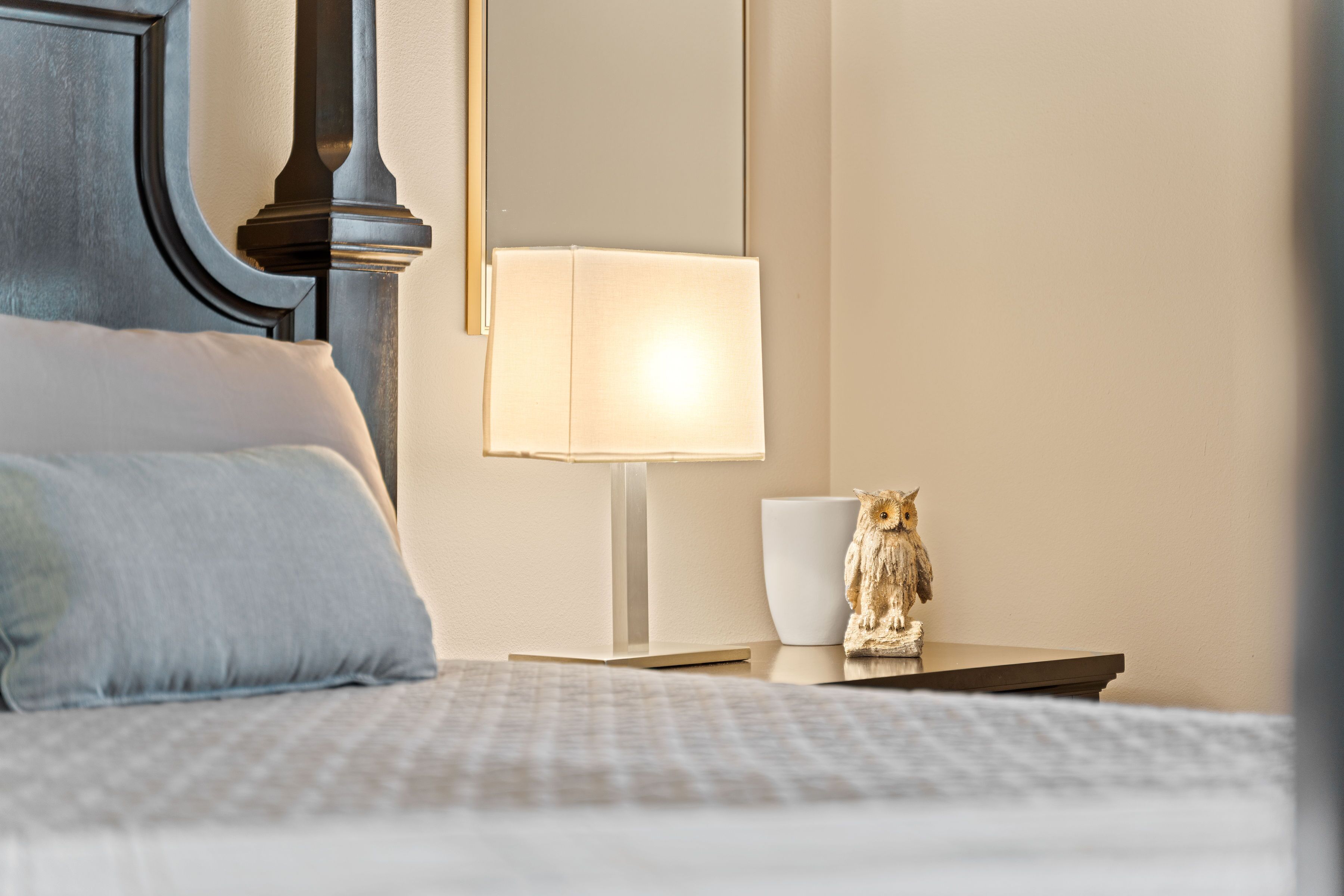 A neatly made bed with a pillow, a bedside lamp, and a small owl figurine on a nightstand.