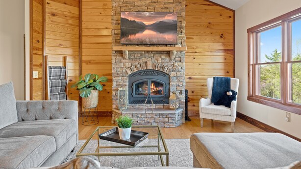 Una sala de estar acogedora con chimenea de piedra, paredes de madera y un amplio ventanal.