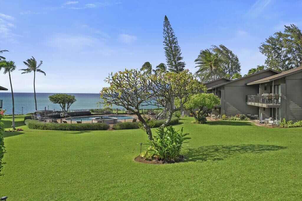 A hotel with a pool, lush green lawn, and a view of the ocean.