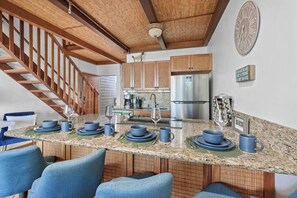 Une cuisine dotée d’un îlot central, d’un escalier en bois et d’une horloge au mur.
