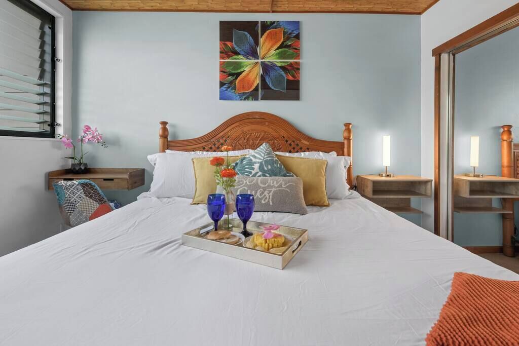 A neatly made bed with a tray of snacks, pillows, and a floral artwork on the wall.