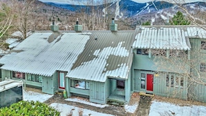 A rustic cabin with a metal roof, a red door, and a view of snow-covered mountains. - Lincoln Escape w/ Deck: 1 Mi to Loon Mountain! (Lincoln)