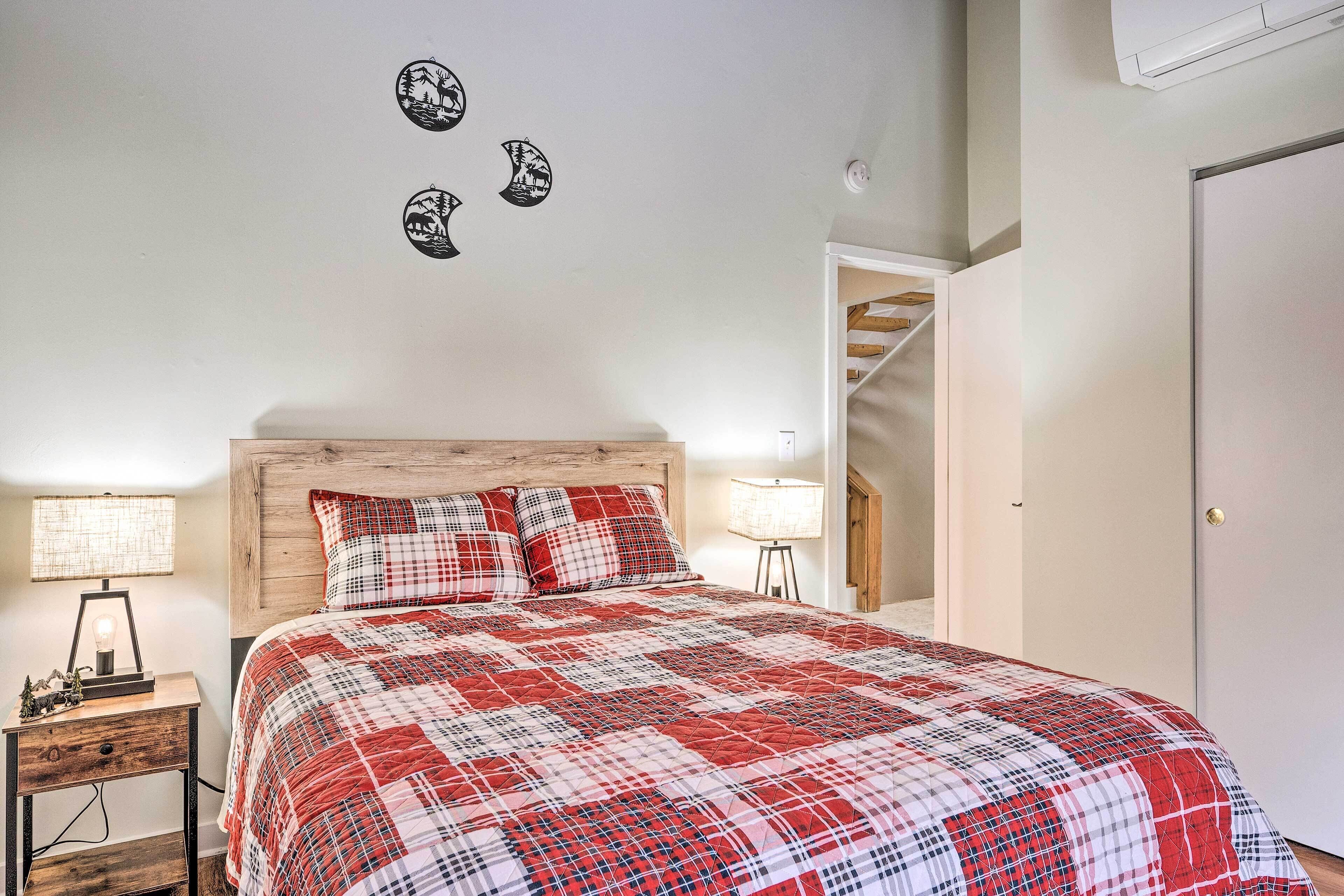 A bedroom with a wooden headboard, a red and white checkered bedspread, two bedside lamps, and a wall-mounted shelf with decorative items.