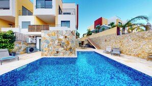 A swimming pool with stone walls and a modern building in the background. - Vila Vida (8) | Private Heated Pool | Sea & Beach | Roof Terrace | Restaurants (Ferragudo)