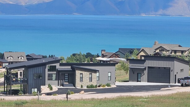 Un barrio residencial con casas modernas, un cielo azul despejado y un lago al fondo.