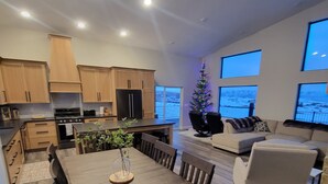 Una cocina moderna con armarios de madera, una mesa de comedor con sillas, un pequeño árbol de Navidad y un amplio ventanal con vistas a un paisaje nevado.