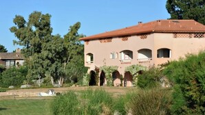 A large, single-story building with a red-tiled roof, arched windows, and a garden area with various plants and a small pond. - Charming duplex apartment "Les pieds dans l'eau" N°7, 70 m from the beach. (Lecci)