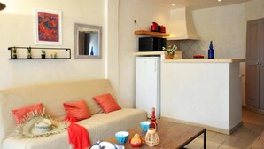 A compact living space with a kitchenette, a sofa with red cushions, a coffee table with various items, and a small refrigerator. - Charming duplex apartment "Les pieds dans l'eau" N°7, 70 m from the beach. (Lecci)