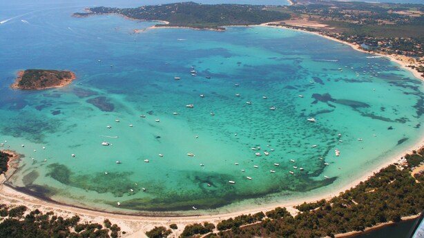 An aerial view of a coastal area with clear turquoise waters, numerous boats, and a sandy beach. - Charming duplex apartment "Les pieds dans l'eau" N°7, 70 m from the beach. (Lecci)