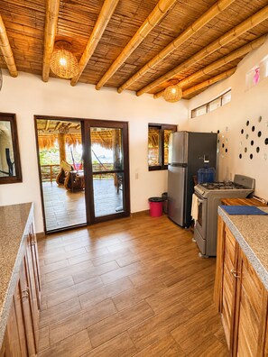 A kitchen with wooden flooring, a gas stove, a refrigerator, and a large window.