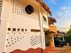 A building with a unique perforated wall design, a thatched roof, and a covered outdoor area with a vehicle.