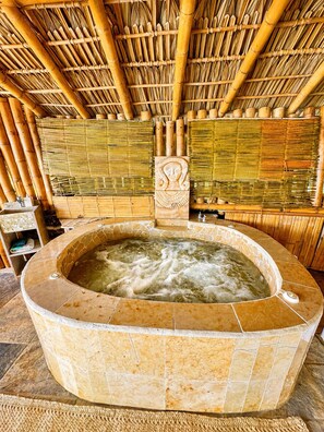 A hot tub with a stone surround, bamboo walls, and a decorative headpiece above it. - Breathtaking Sea View Apartment Casa Xochi (San Agustinillo)