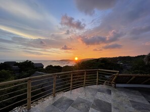 A sunset view from a balcony with a stone floor and bamboo railing. - Breathtaking Sea View Apartment Casa Xochi  (San Agustinillo)