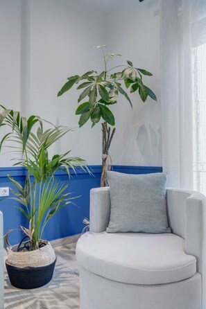 Una habitación con un sillón blanco, una pared azul decorativa y dos plantas en macetas.
