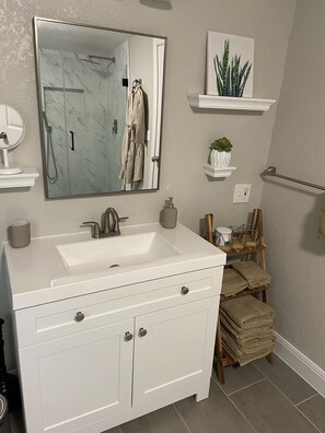 Une salle de bain avec un meuble-lavabo blanc, un grand miroir, un évier et un porte-serviettes.