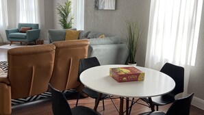 Ein modernes Wohnzimmer mit einem runden Tisch, mehreren Stühlen, einer Couch und einem Catan-Brettspiel.