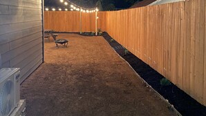 Ein Garten mit Holzzaun, einer Terrasse und Lichterketten.