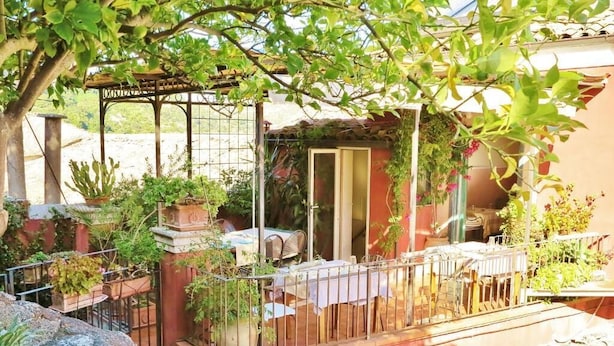 Un patio extérieur couvert, aménagé avec une table et des chaises, entouré de plantes en pot et délimité par une clôture en métal.