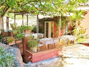 Un patio techado al aire libre con una mesa y sillas, rodeado de macetas con plantas y una cerca de metal.