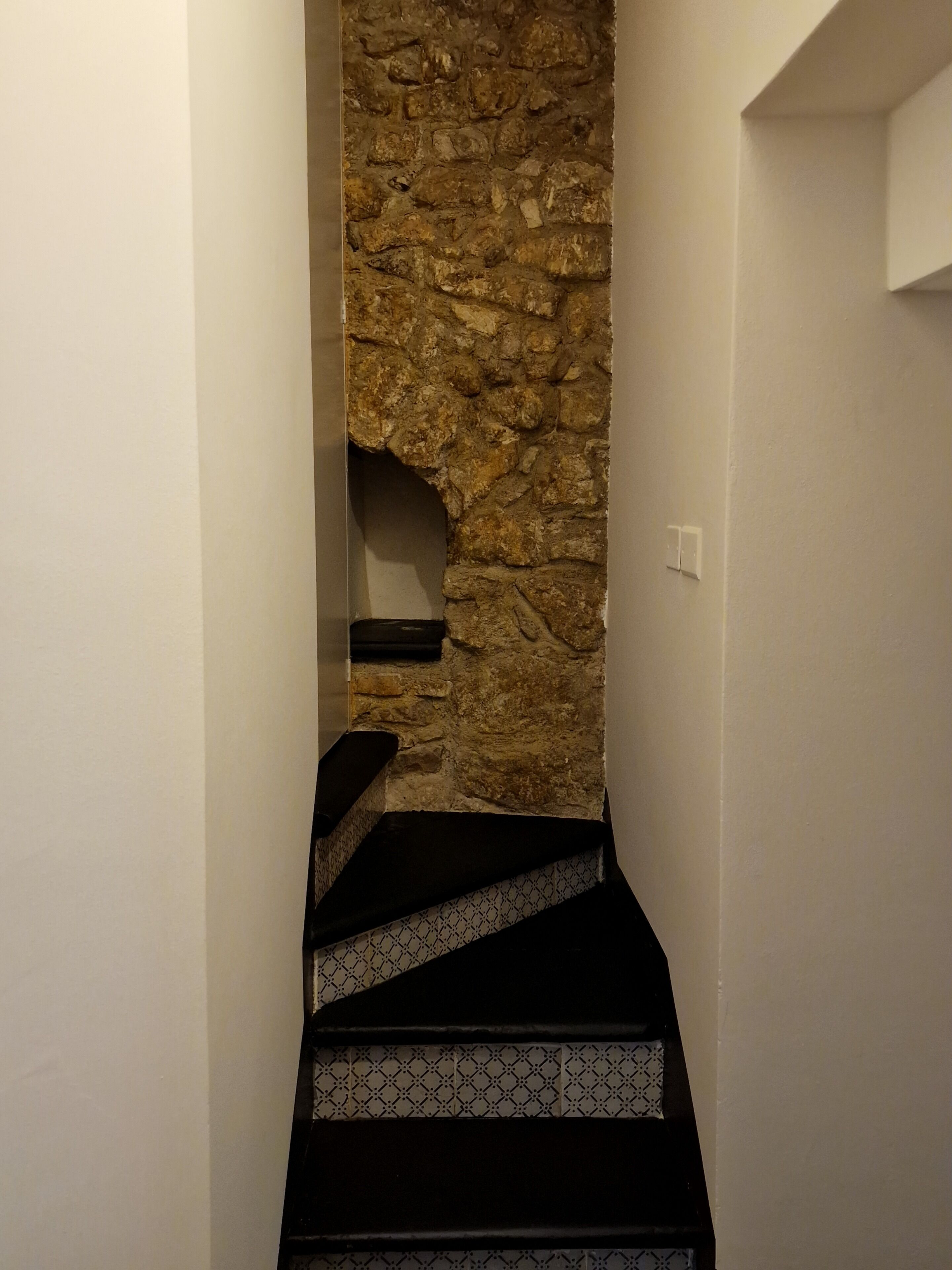A narrow stairway with a stone wall on one side and a black and white patterned step on the other.