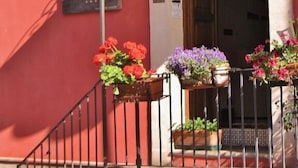 Un bâtiment à la façade rouge, doté d’un balcon avec des balustrades en métal et de jardinières contenant des fleurs rouges et violettes.