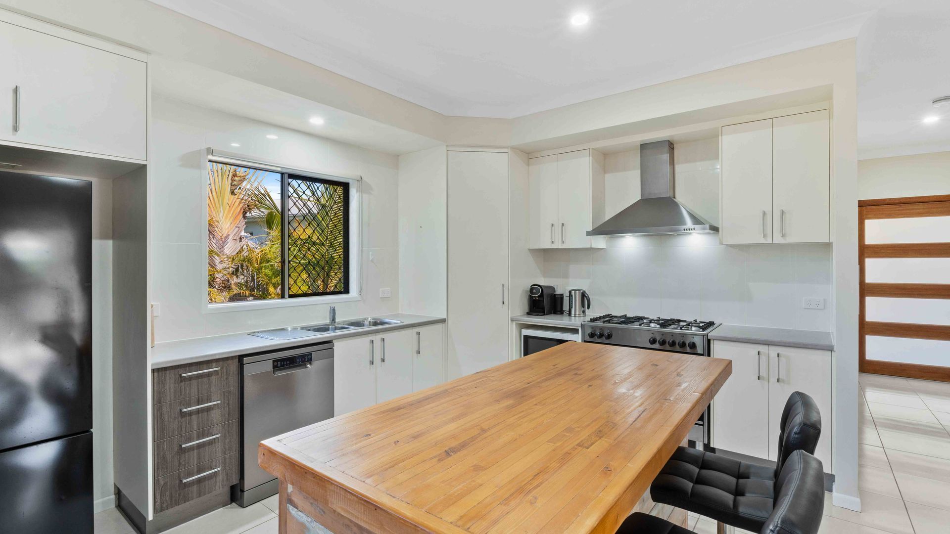 A modern kitchen with a wooden dining table, stainless steel appliances, and white cabinetry.