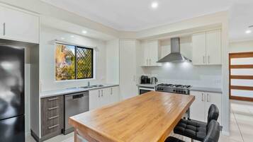 A modern kitchen with a wooden dining table, stainless steel appliances, and white cabinetry.