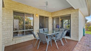 Eine überdachte Terrasse mit einem Glastisch und Stühlen, Backsteinwänden und einem Deckenventilator.
