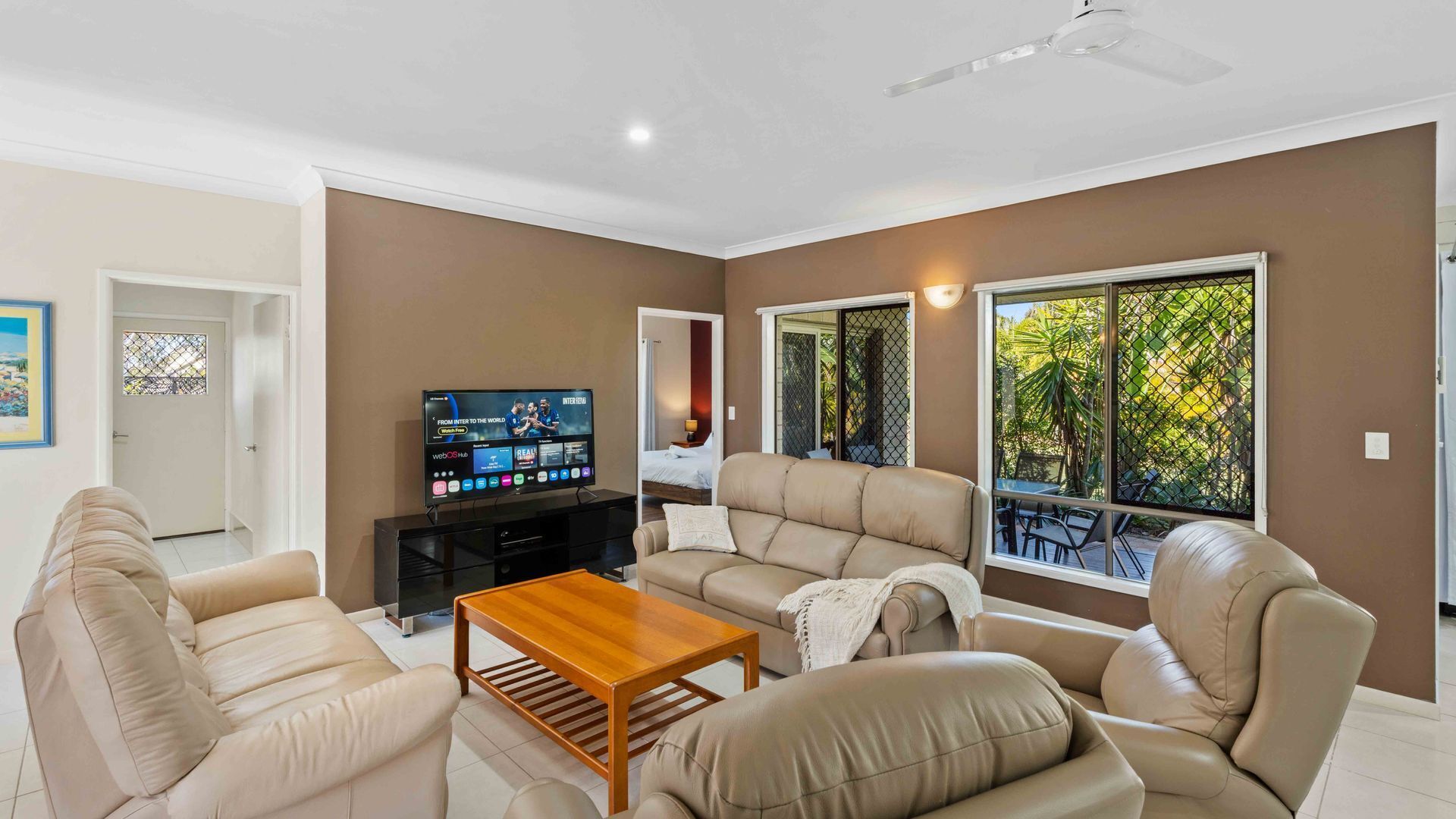 A living room with a television, leather sofas, a wooden coffee table, and a ceiling fan.