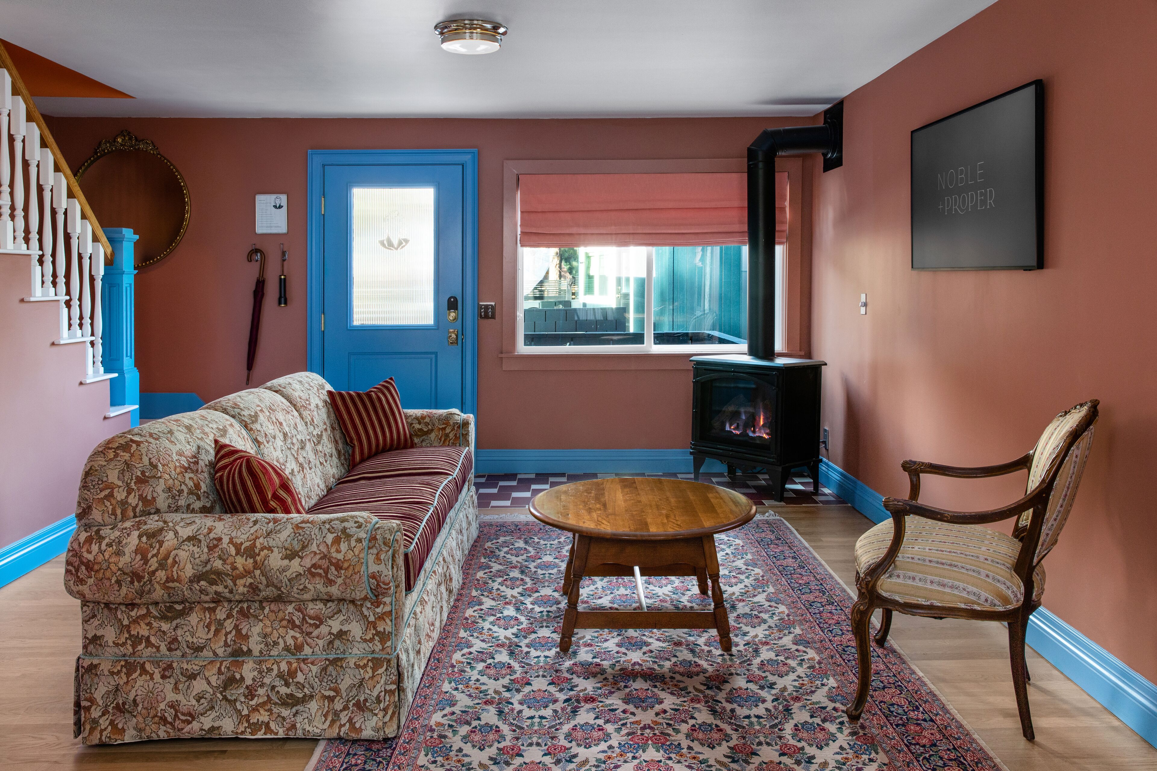 Una sala de estar con una puerta azul, un sofá estampado, una mesa de centro de madera y una silla.
