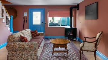 Una sala de estar con una puerta azul, un sofá estampado, una mesa de centro de madera y una silla.