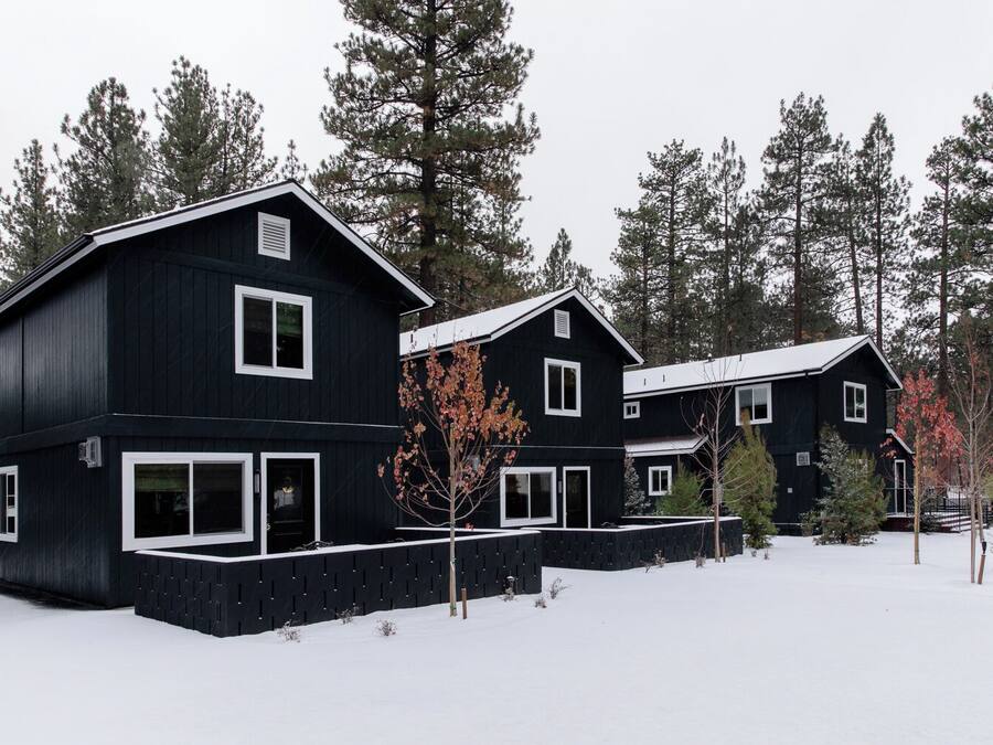 A black two-story house with white trim, surrounded by snow and trees.