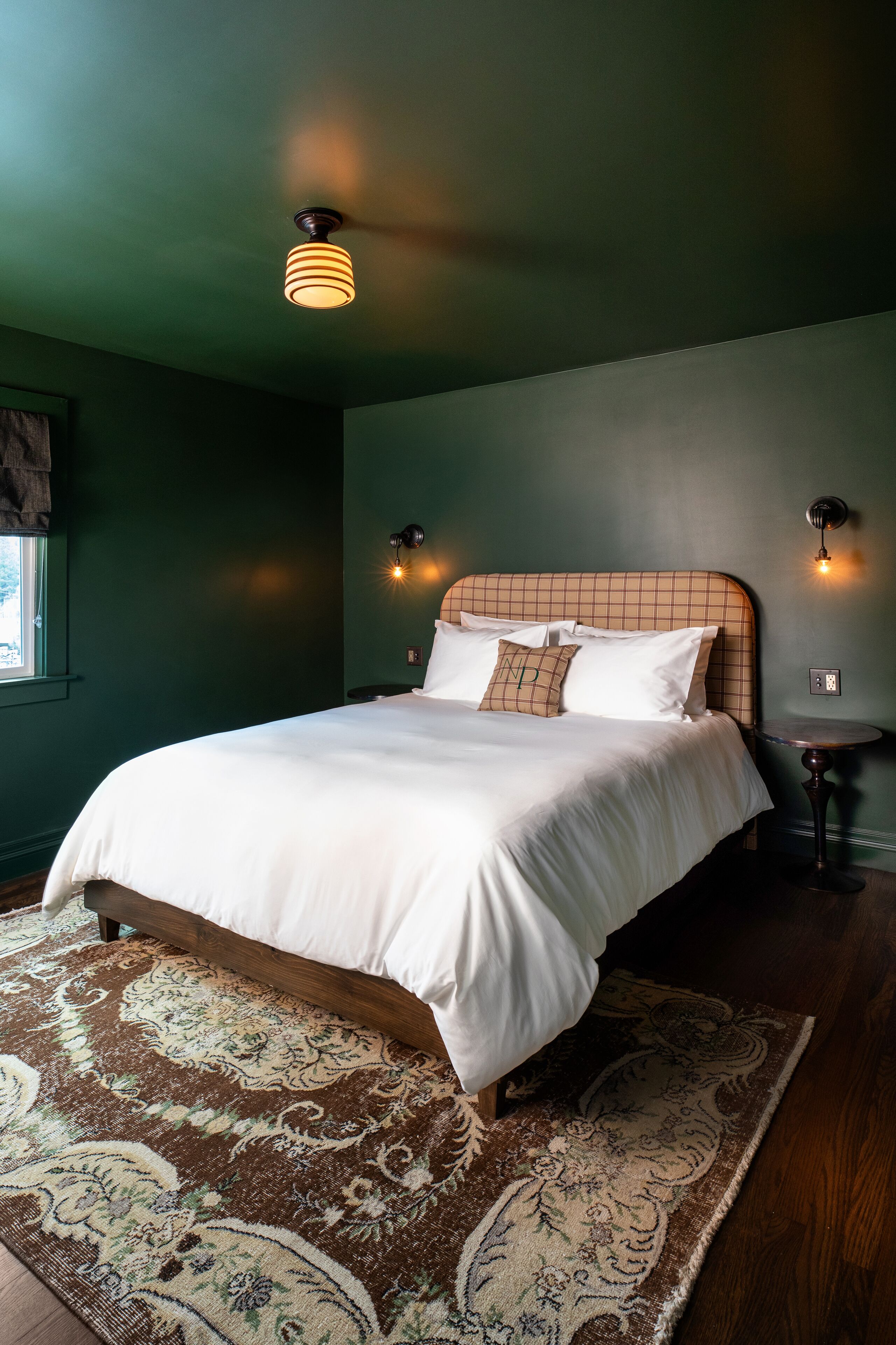 A neatly made bed with a checkered headboard, a patterned rug, and two wall-mounted light fixtures.