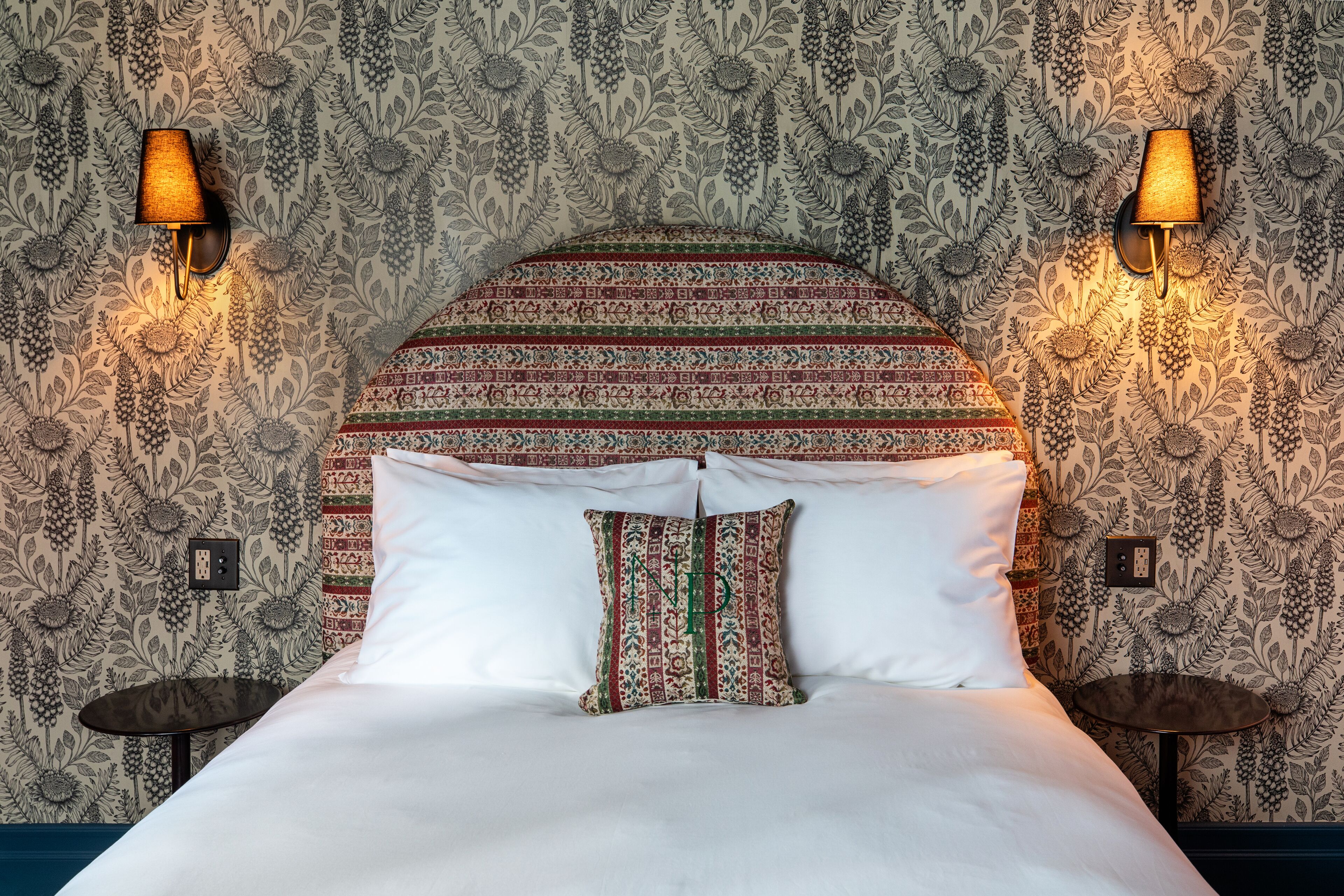 A bed with a patterned headboard, two bedside tables, and wall-mounted lamps.