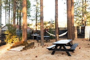 A picnic area with a wooden table and benches, surrounded by tall trees and a hammock. - N+P Boutique Lodge (Big Bear Lake)