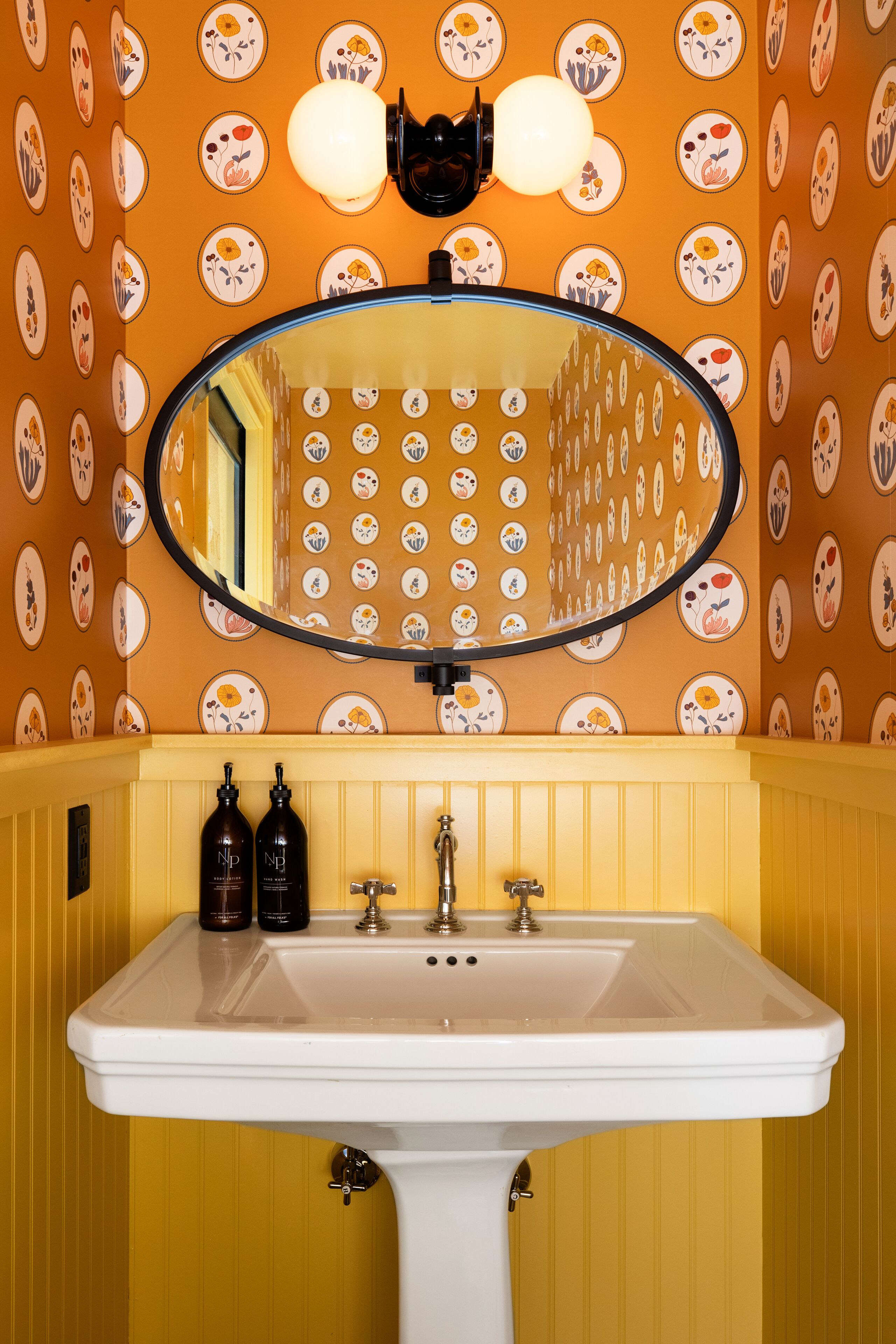 Une salle de bain avec un lavabo blanc, deux bouteilles noires et un miroir au-dessus.