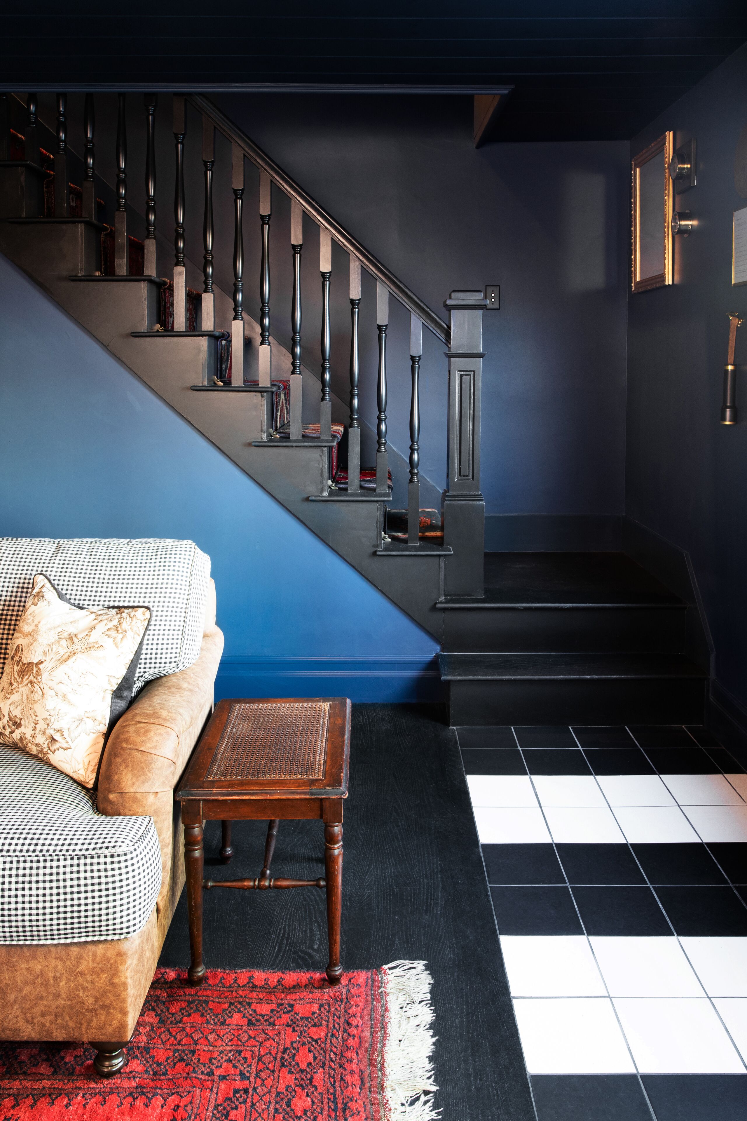 A modern living room with a sofa, a coffee table, a patterned rug, a staircase with a blue accent wall, and a black and white tiled floor.