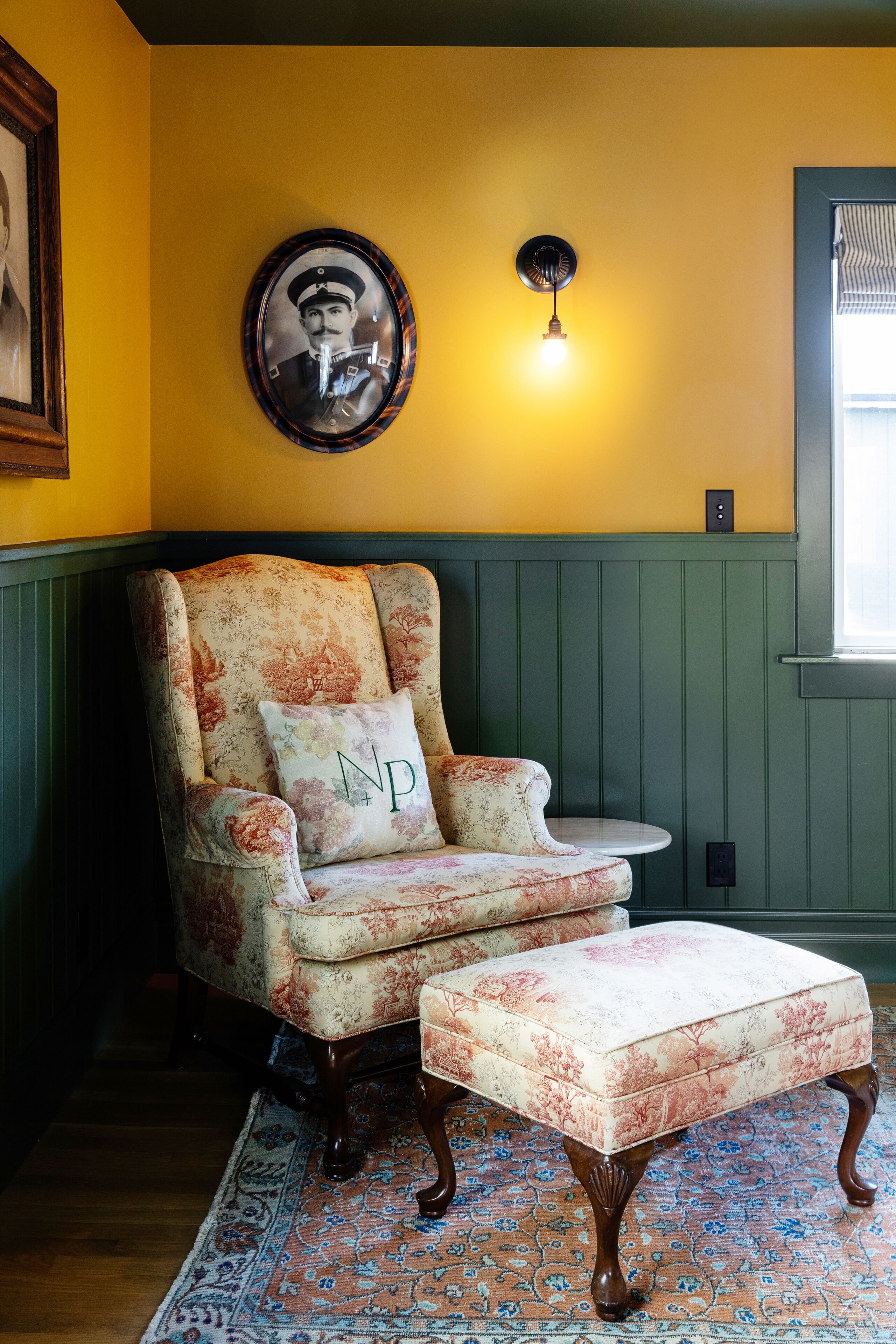 Un fauteuil traditionnel recouvert d’un tissu à motifs floraux, accompagné d’un pouf assorti, le tout placé sur un tapis à motifs.