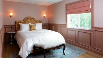 A bedroom with a large bed, two bedside tables, a window with a view, and wall sconces.