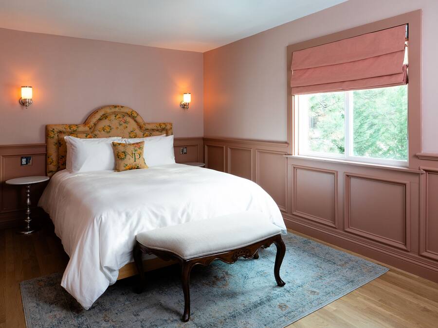 A bedroom with a large bed, two bedside tables, a window with a view, and wall sconces.