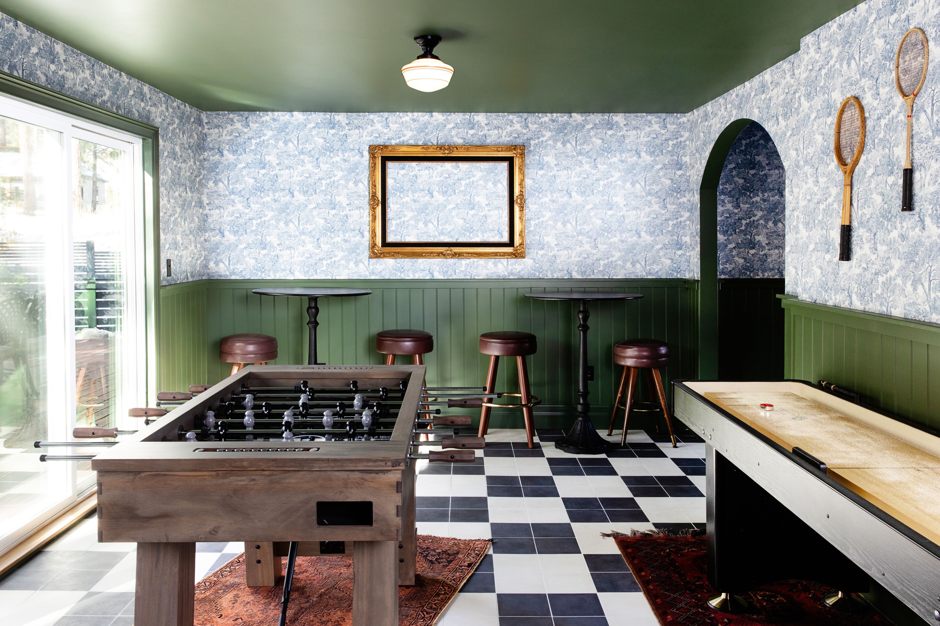 A room with a foosball table, a pool table, and a bar area with stools.